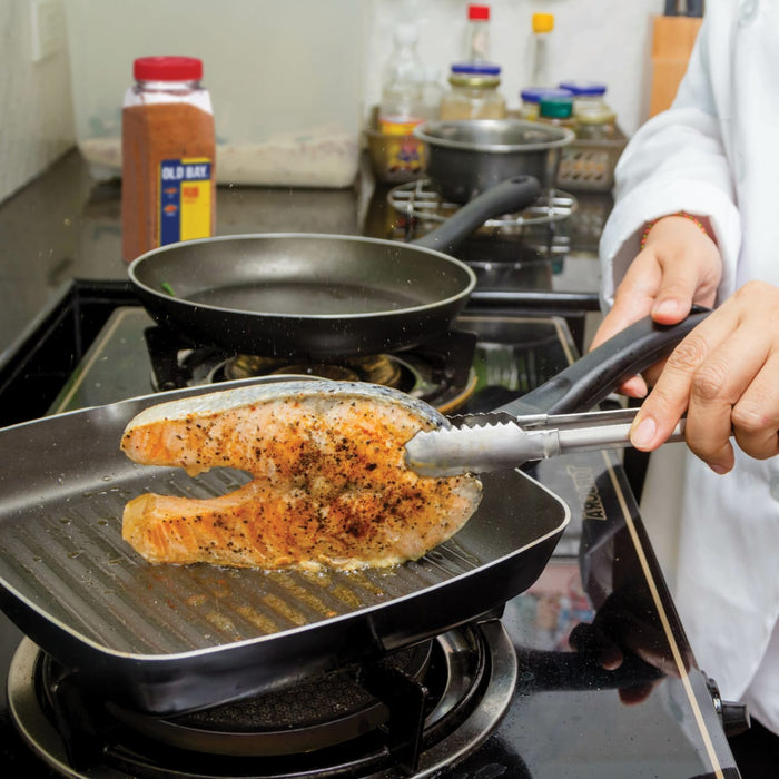 A person uses tongs to flip a piece of salmon in a grill pan.