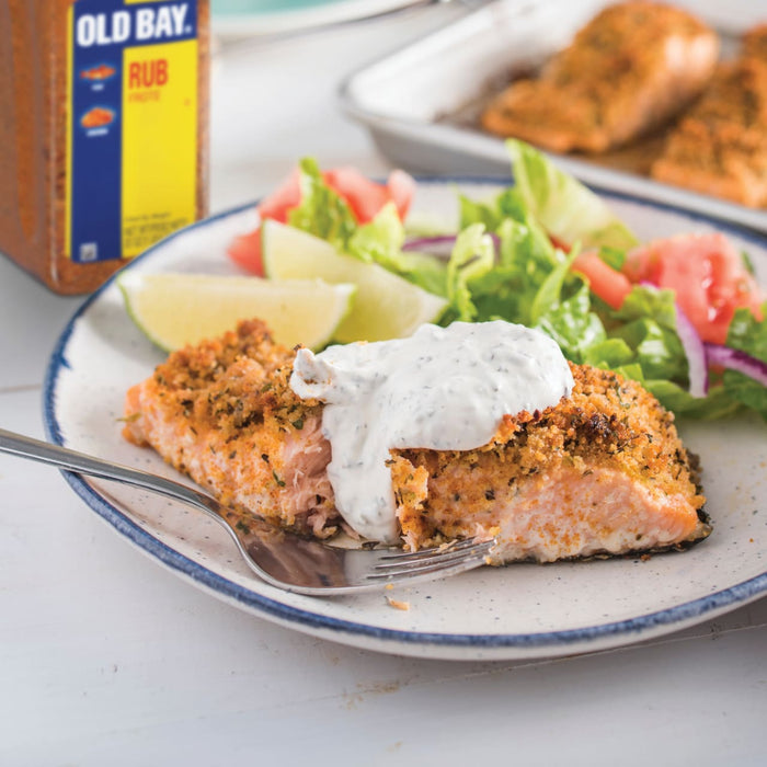 A plate of Old Bay Rub crusted salmon with a side salad and a dollop of creamy sauce.