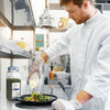 A chef in a white uniform is pouring a dressing over a salad using McCormick Culinary Dill Weed.