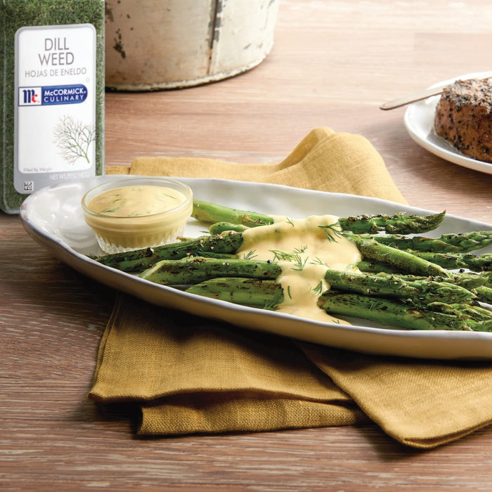 A plate of asparagus spears drizzled with a creamy dill sauce with a jar of McCormick Culinary Dill Weed in the background.