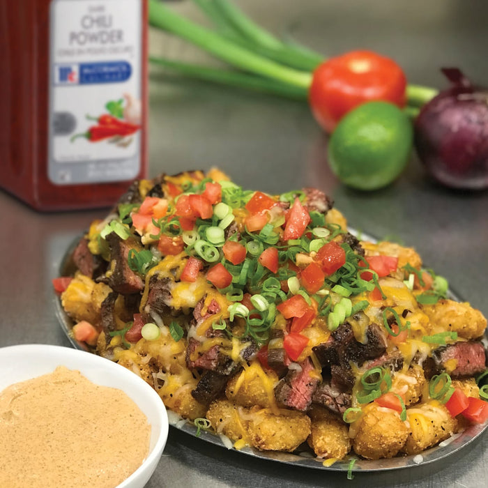 A plate of tater tots topped with steak cheese tomatoes and green onions.
