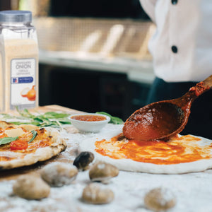 A person is adding tomato sauce to a pizza dough with a wooden spoon.
