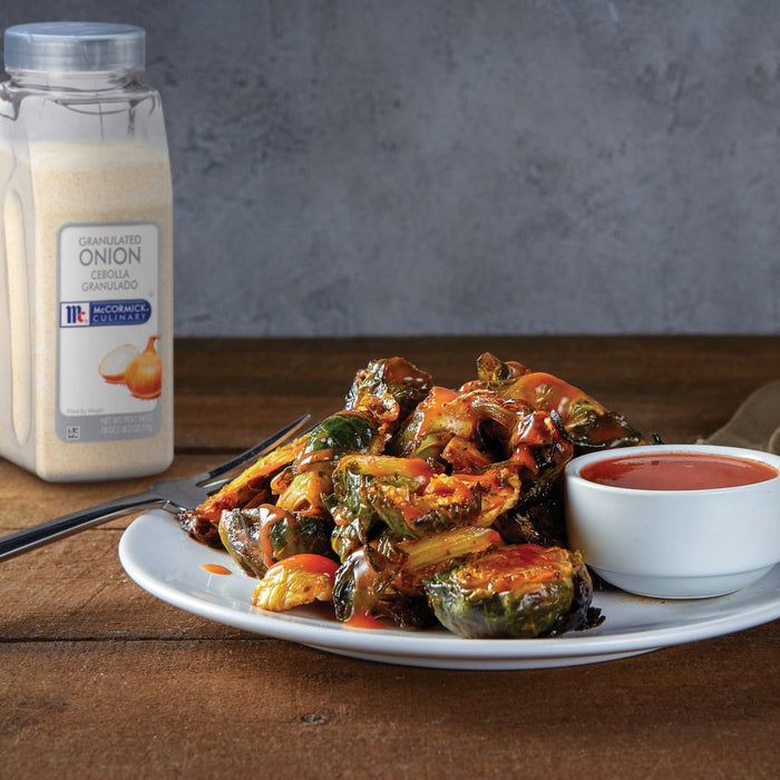 A plate of McCormick Culinary Granulated Onion seasoned Brussels sprouts with a side of hot sauce.