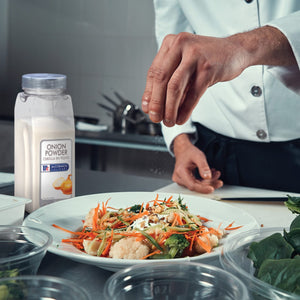 A chef is sprinkling McCormick Culinary Onion Powder on a salad.