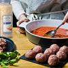 A person is preparing a meal with McCormick Culinary Minced Onion tomato sauce and meatballs.