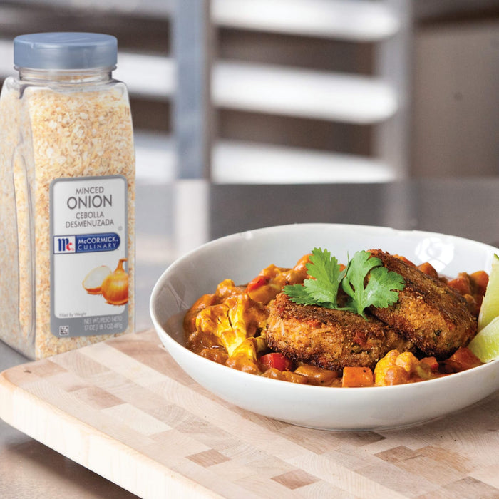 A container of McCormick Minced Onion next to a bowl of curry with cauliflower and fried patties.