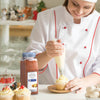 A chef is decorating a cupcake with frosting while holding a jar of McCormick Culinary Ground Nutmeg.