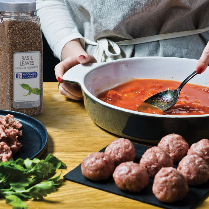 A person is preparing a meal with McCormick Culinary Basil Leaves ground meat and tomato sauce.