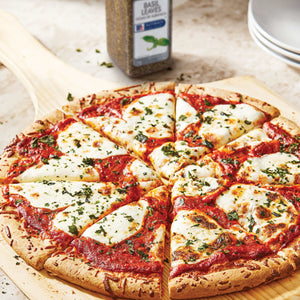 A pizza with mozzarella cheese and tomato sauce on a wooden cutting board with a jar of McCormick Basil Leaves.