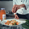 A chef is sprinkling McCormick Culinary Salad Supreme Seasoning on a salad.