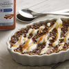A close-up of a small white ramekin filled with a creamy dessert topped with caramel and a McCormick Culinary Ground Cinnamon label.