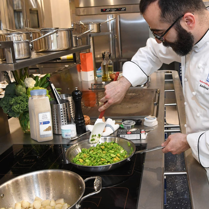 A chef is cooking fava beans in a pan on a stovetop using a spatula to stir them.