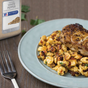 A plate of food with a piece of grilled fish on top of a bed of pasta with a McCormick Culinary Ground White Pepper container in the background.