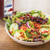 A bowl of salad with bacon bits cucumbers tomatoes and red onion with a jar of McCormick Culinary Bacon Flavored Bits in the background.