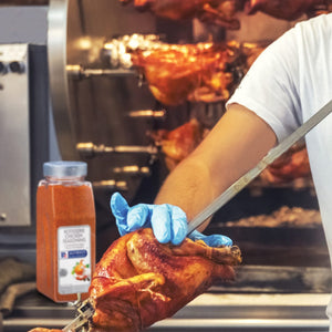 A person wearing blue gloves is holding a roasted chicken in front of a rotisserie with a jar of McCormick Rotisserie Chicken Seasoning.
