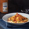 A plate of shrimp and grits with bacon and green onions with a jar of McCormick Bayou Cajun Seasoning in the background.