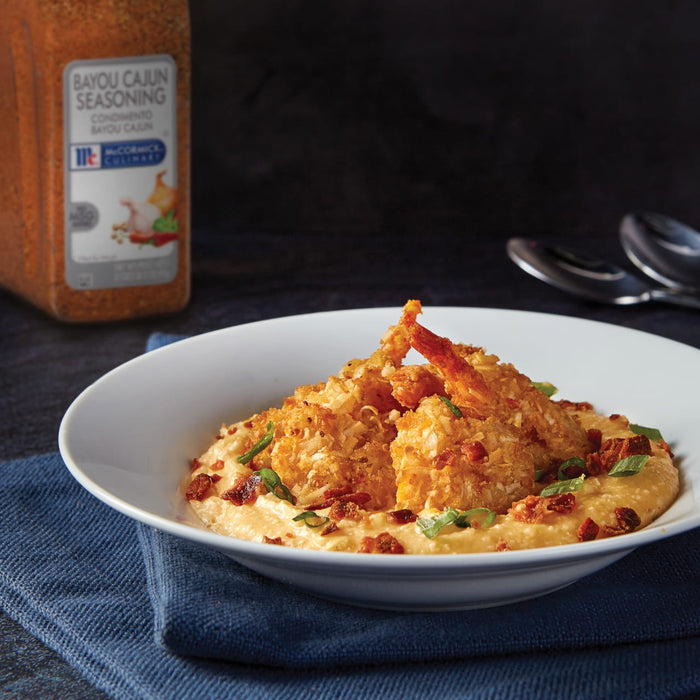 A plate of shrimp and grits with bacon and green onions with a jar of McCormick Bayou Cajun Seasoning in the background.
