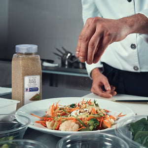 A chef is seasoning a salad with McCormick Culinary Pure Ground Black Pepper.