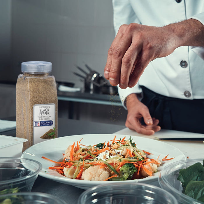 A chef is seasoning a salad with McCormick Culinary Pure Ground Black Pepper.