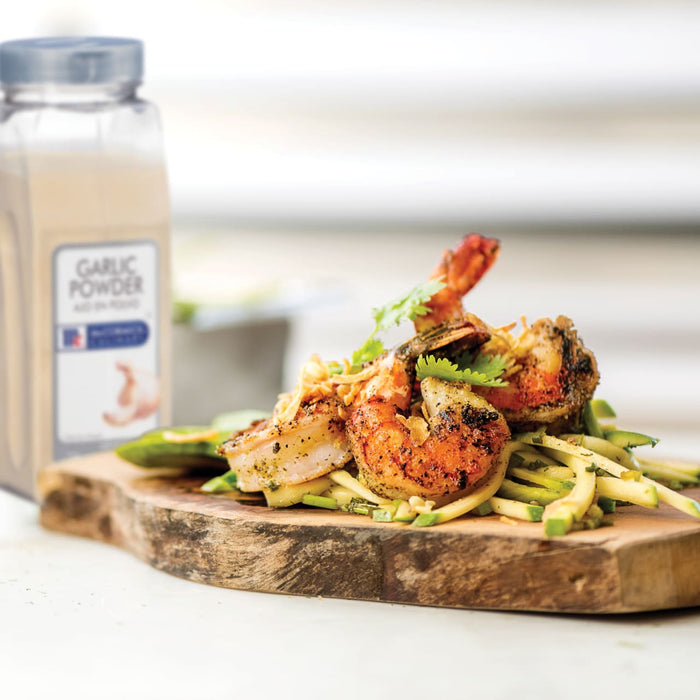 Grilled shrimp with zucchini noodles on a wooden cutting board next to a container of McCormick Garlic Powder.
