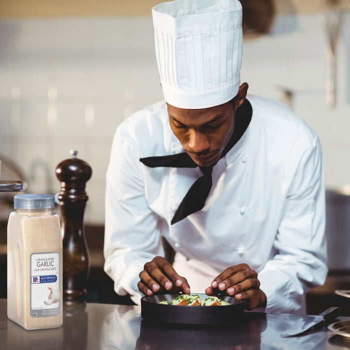 A chef in a white uniform is plating a dish of food with a jar of McCormick Culinary Granulated Garlic in the foreground.