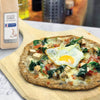 A close-up of a pizza with spinach chicken bacon and a fried egg on a wooden cutting board next to a McCormick Culinary Granulated Garlic container.