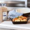 A small cast iron dish filled with a cheesy casserole topped with green onions and red pepper flakes next to a jar of McCormick Culinary Minced Garlic.