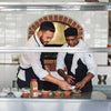 Two chefs prepare food in a kitchen one is holding a small white bowl and the other is holding a bottle of Lawrys Garlic Powder.