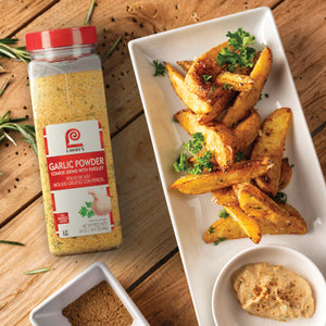 A jar of Lawrys Garlic Powder next to a plate of seasoned potato wedges and a small bowl of dip.