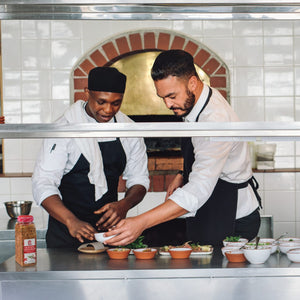 Two chefs in a kitchen preparing food one is holding a bowl of Lawrys Cracked Pepper Garlic &amp; Herb Rub.