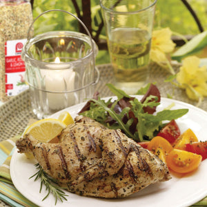 A plate of grilled chicken with lemon wedges tomatoes and a sprig of rosemary.