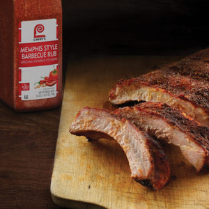 A jar of Lawrys Memphis Style Barbecue Rub next to a wooden cutting board with three ribs of pork.