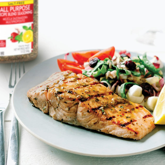 A plate of grilled salmon with a side salad and a lemon wedge with a jar of Salt Free All Purpose Recipe Blend Seasoning in the background.
