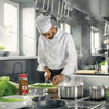 A chef in a white uniform prepares a meal in a kitchen with a Lawrys Lemon &amp; Pepper Seasoning bottle on the counter.