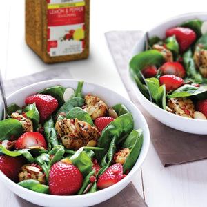 A bowl of salad with spinach strawberries chicken and almonds.