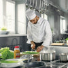 A chef in a white uniform is preparing a meal in a kitchen with a pot of boiling water on the stove.