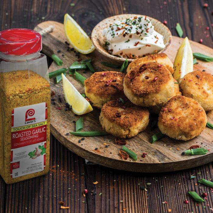 A jar of Lawrys Touch of Sea Salt Roasted Garlic Seasoning next to a plate of fried food.