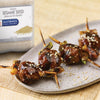 McCormick Culinary Whole Sesame Seed is shown next to a plate of grilled meat skewers topped with sesame seeds.