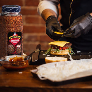 A person is preparing a hamburger with McCormick Grill Mates Hamburger Seasoning.