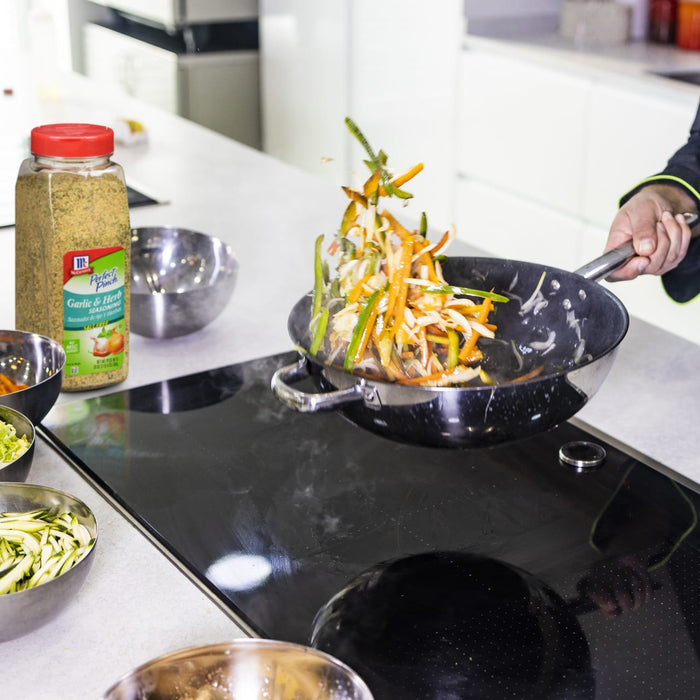 A person is cooking vegetables in a pan on a stovetop using McCormick Perfect Pinch Garlic &amp; Herb seasoning.