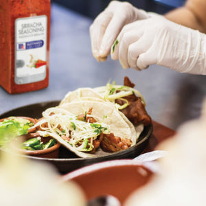 A close-up of a plate of tacos with a jar of McCormick Sriracha Seasoning in the background.