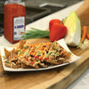 A plate of wonton chips topped with shredded cabbage carrots red peppers and a sriracha sauce.