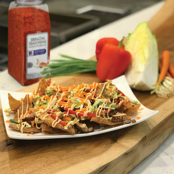 A plate of wonton chips topped with shredded cabbage carrots red peppers and a sriracha sauce.