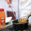 A person is using tongs to remove french fries from a pot of hot oil with a bottle of RedHot Original Seasoning in the foreground.