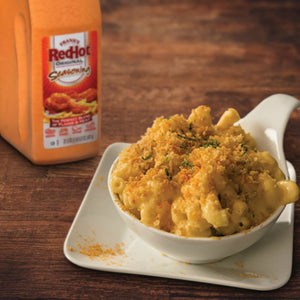 A bowl of macaroni and cheese with a bottle of Franks RedHot Original Seasoning in the background.