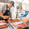 A man is seasoning ribs with Cattlemens BBQ sauce.