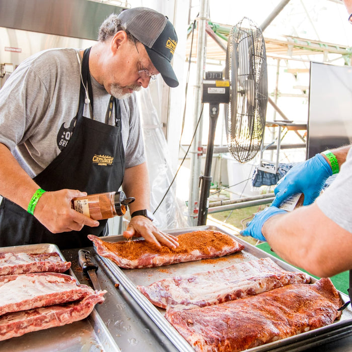 A man is seasoning ribs with Cattlemens BBQ sauce.