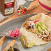 A close-up of a pulled pork taco with avocado radish and pickled jalapeno with Cattlemens BBQ Rub in the background.