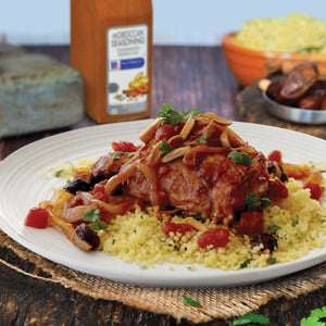 A plate of Moroccan chicken with couscous tomatoes onions and almonds.