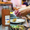A hand holds chopsticks over a plate of Japanese food with a jar of McCormick Japanese Seven Spice in the background.